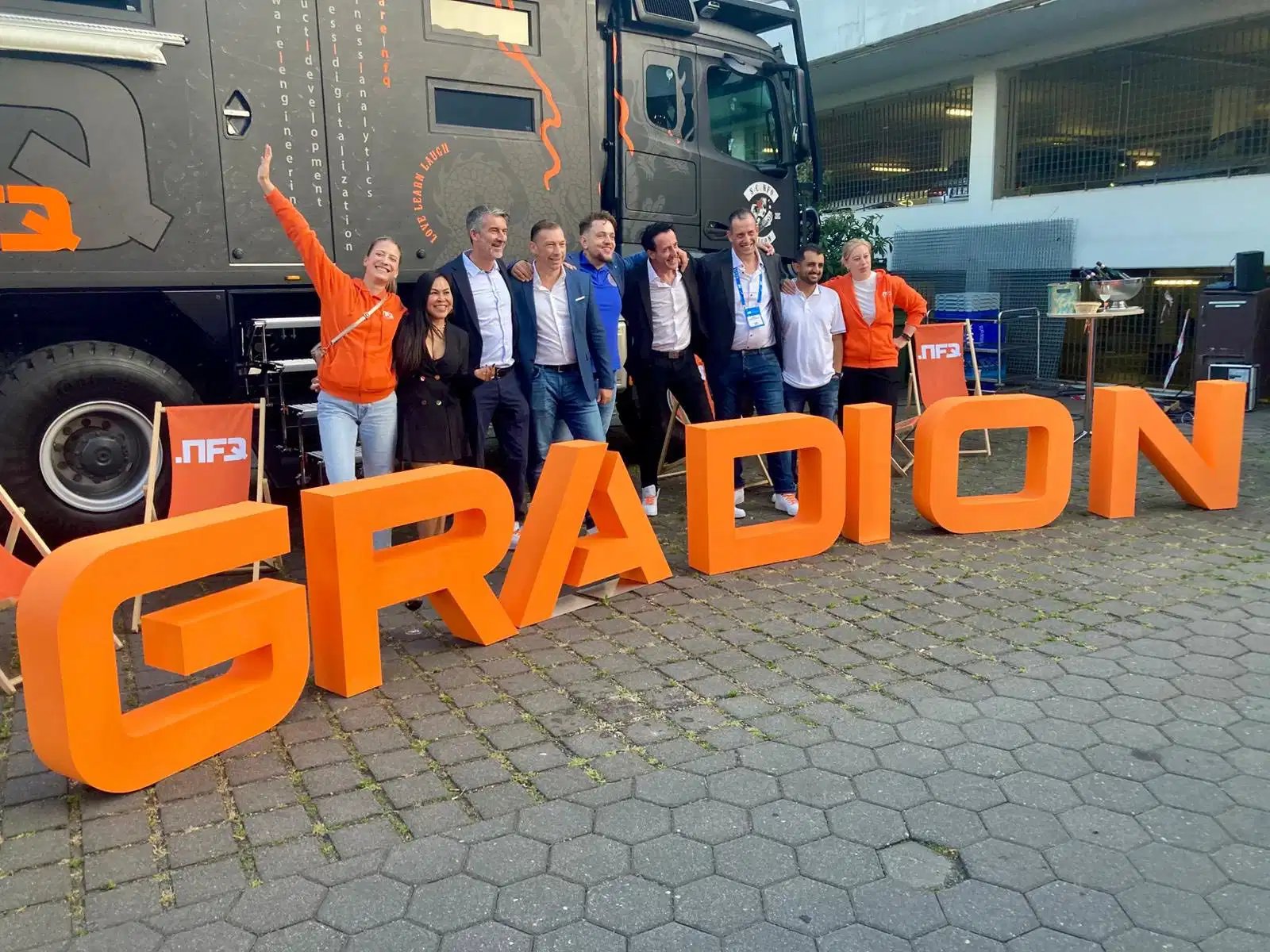 Group of people standing behind large orange GRADION letters, celebrating in front of a bus