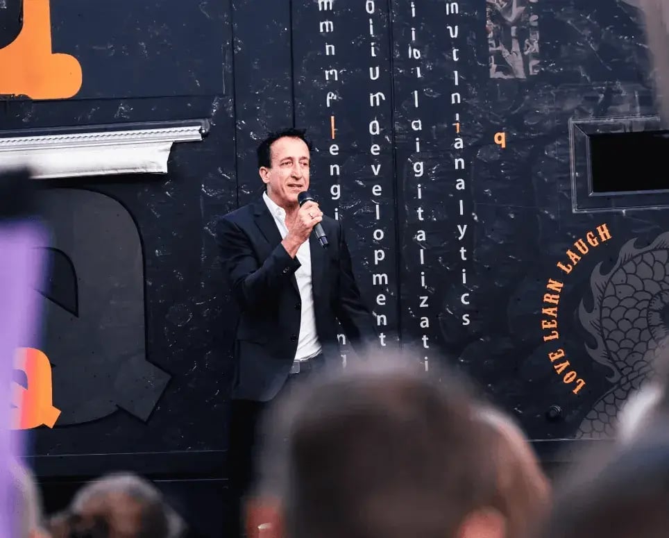 A man in a black suit holding a microphone and speaking.